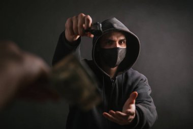 Kapüşonlu ve maskeli bir gangster karanlık bir arkaplanda elinde bir silah tutuyor ve kurbandan para alıyor. Haydut silahını doğrultur ve dolar ister..