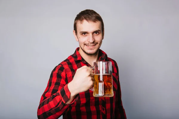 白い背景に泡のないビールの大きなマグカップを持っている小細工の赤いシャツの若い男 酒が悪い — ストック写真