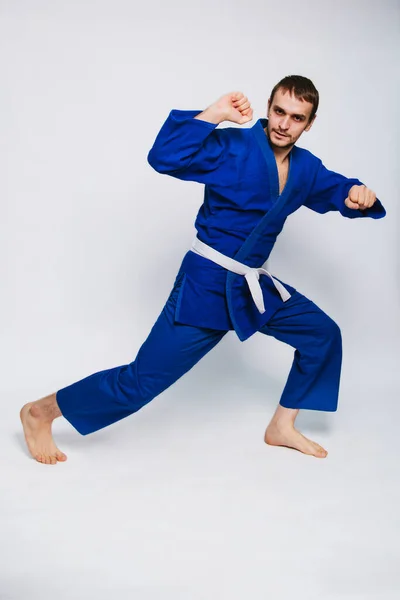 Young man in a blue kimono on a white background. The guy is a beginner in martial arts. studio photo