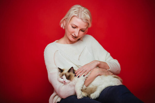 Young woman hugs a ragdoll cat on a red background. Love to the animals. Studio photo