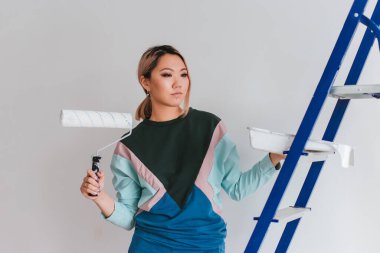 Asyalı görünümlü bir kız evini onarıyor. Genç bir kadın duvarı beyaza boyuyor. Evde konfor oluşturur