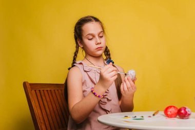 Pembe elbiseli bir kız Paskalya bayramı için yumurta boyuyor..