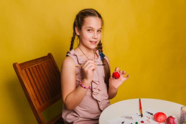 Pembe elbiseli bir kız Paskalya bayramı için yumurta boyuyor..