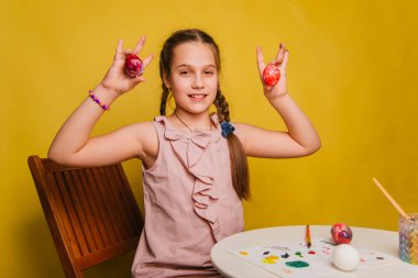 Pembe elbiseli bir kız Paskalya bayramı için yumurta boyuyor..