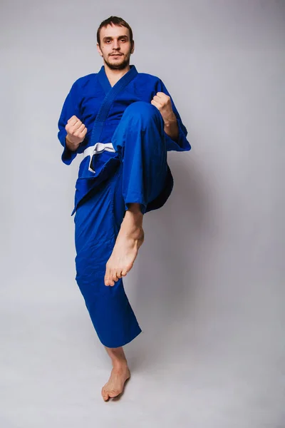 Young man in a blue kimono on a white background. The guy is a beginner in martial arts. studio photo