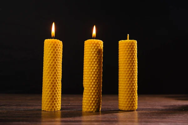 Three yellow beeswax candles are on the table. Eco product on a dark background