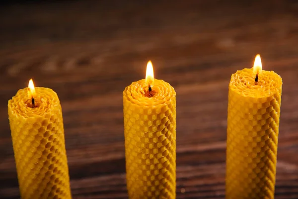Three yellow beeswax candles are on the table. Eco product on a dark background