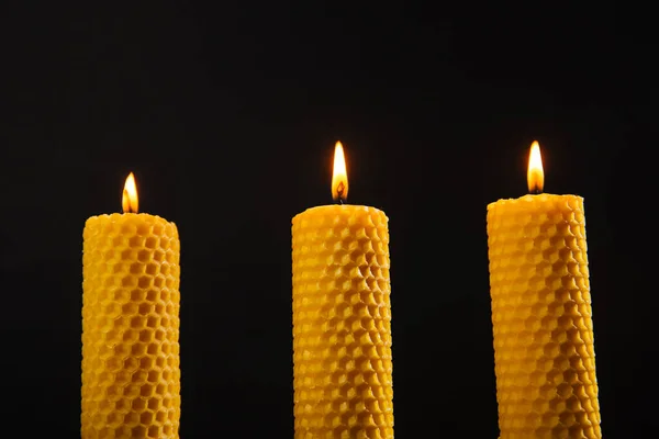 Three yellow beeswax candles are on the table. Eco product on a dark background