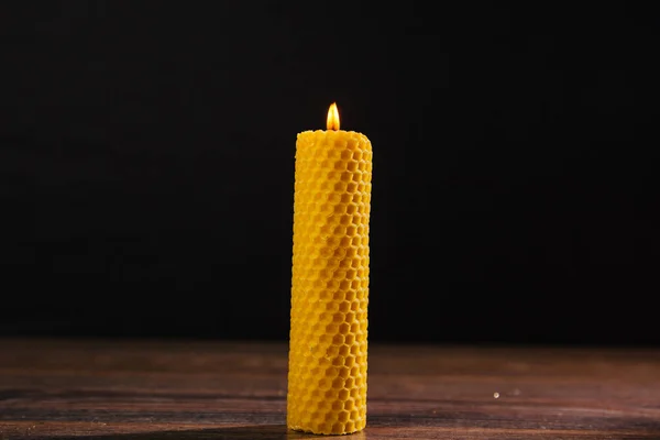 a yellow beeswax candle stands on the table. Eco product on a dark background