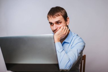 Mavi gömlekli genç yakışıklı bir adam bilgisayarın başında oturuyor. Beyaz arka planda çalışan bir ofis çalışanı bir dizüstü bilgisayar için çalışır. izole et