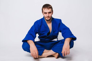 Mavi kimonolu, beyaz kuşaklı bir adam yerde oturuyor. Doğulu dövüş sanatlarının acemi bir dövüşçüsü.