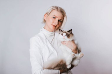 Beyaz önlüklü bir kız tüylü bir Regg Dol kedisi tutuyor. Veterenar hayvanı tarıyor. Hayvan bakımı