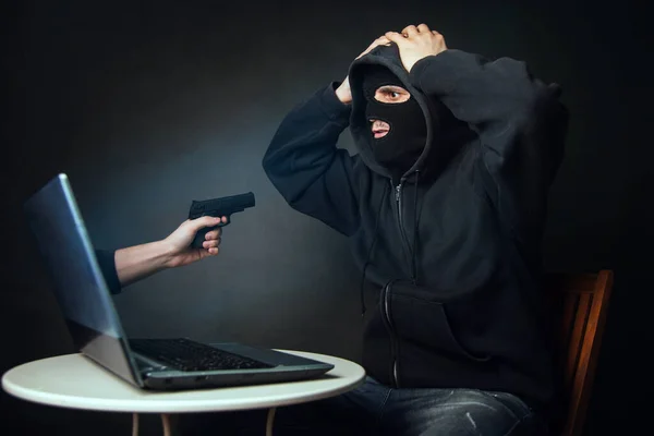 インターネット詐欺師を捕まえた デジタル強盗の写真概念です 仮面の男はラップトップからピストルで手を恐れている — ストック写真