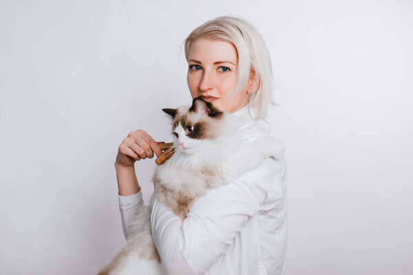 A girl in a white coat is holding a fluffy cat regg dol. Veterenar is combing the animal. Pet care