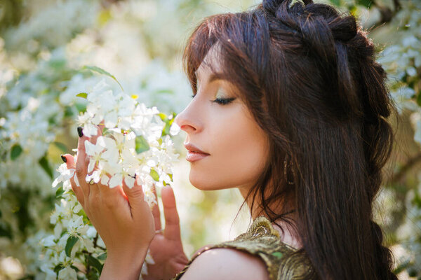 Portrait of a beautiful girl with long hair among the apple trees.Woman sniffing flowers