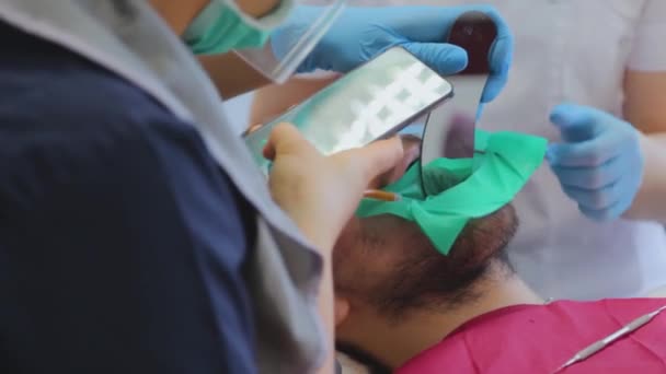 El dentista toma fotos de los dientes de los pacientes usando un teléfono inteligente. El tipo en la cita con el dentista.Tratamiento dental — Vídeos de Stock