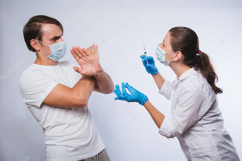 People vaccination phobia concept. A female doctor is trying to vaccinate a frightened male patient. The mistrustful patient, the anti-inoculant refuses to take it. Stop vaccination. No coronavirus vaccines.