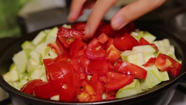Egy női kéz zöldségeket tesz egy fekete serpenyőbe, cukkinit, répát, paradicsomot, paprikát dobál. Főzés otthon. — Stock videók