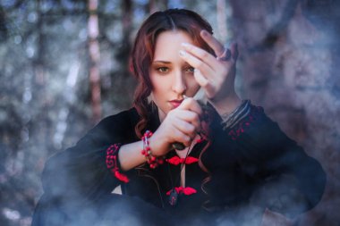 Slav tarzı uzun siyah elbiseli bir cadı dağlarda sihirli bir ayin düzenliyor. Karanlık bir ormanda büyülenmiş bir kadın..