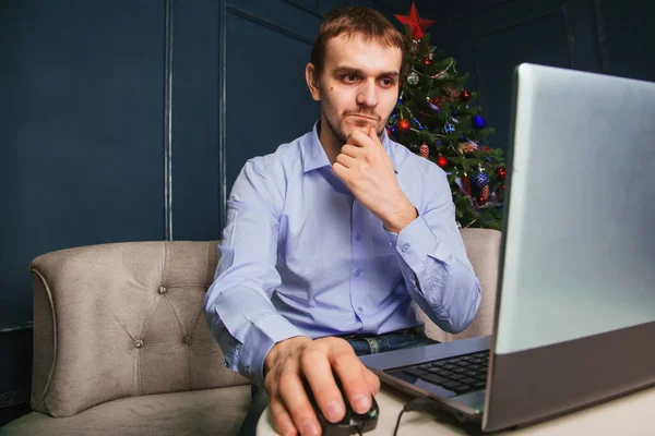 Mavi Tişörtlü Bir Adam Dizüstü Bilgisayarın Başında Yeni Yıl Ağacının — Stok fotoğraf