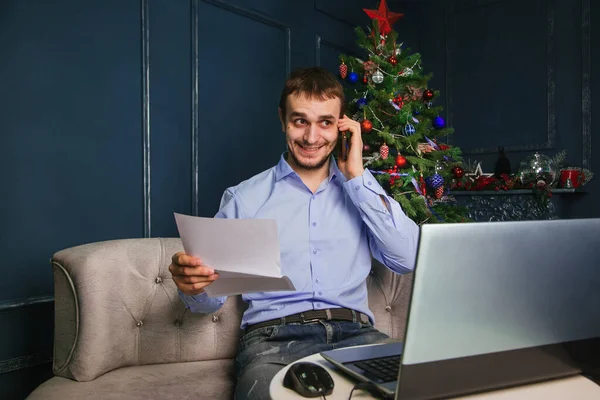 Mavi Gömlekli Bir Adam Dizüstü Bilgisayarın Başına Oturur Telefonda Noel — Stok fotoğraf