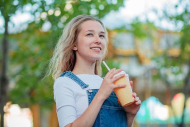 Kot elbise giymiş genç bir kadın bir lunaparktaki dondurma şeklinde bir bardak kahveyle ayakta duruyor. Modern elbiseli kız atlıkarıncada kokteyl içiyor.