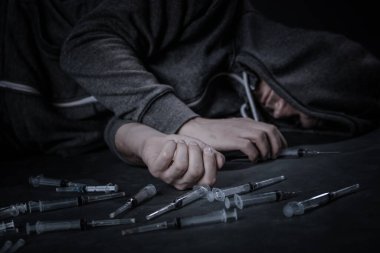 Uyuşturucu bağımlısı biri şırıngaya bir doz ilaç koyar. Adam bir bağımlı, uyuşturucuyla mücadele kavramı. Genç bir adam kullanılmış şırıngaların arasında oturuyor..