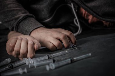 Uyuşturucu bağımlısı biri şırıngaya bir doz ilaç koyar. Adam bir bağımlı, uyuşturucuyla mücadele kavramı. Genç bir adam kullanılmış şırıngaların arasında oturuyor..