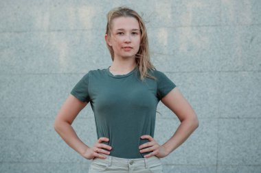 Siyah turkuaz tişörtlü genç bir kadın sokakta gri bir duvara karşı duruyor. Boş elbiseli kız. Model.