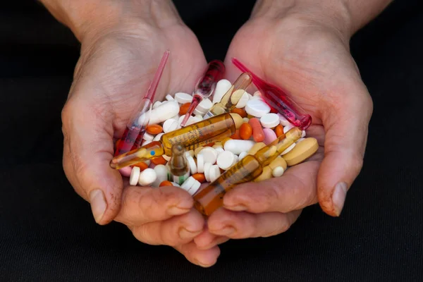 A handful of various pills in female hands over black background