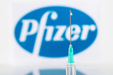 Teo, İspanya; 21 Aralık 2020: Pfizer Covid-19 aşı konsepti Bir şırınga ve üzerinde bir damla sıvı bulunan Pfizer şirketi logosu arka planda bulanıklaştı.