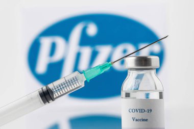 Teo, İspanya; 21 Aralık 2020: Pfizer Covid-19 aşı konsepti Bir şırınga ve bir şişe yakın plan, Pfizer şirket logosu arka planda bulanıklaştı.