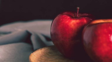 Ahşap bir tabakta iki kırmızı elma ve siyah arka planda gri bir masa örtüsü. Tabloya benzeyen minimalist bir görüntü. Metin için kopyalama alanı olan basit bir natürmort.