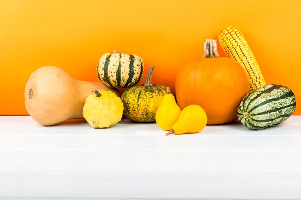 Kürbisse isoliert auf weißem Holztisch und orangefarbenem Hintergrund — Stockfoto