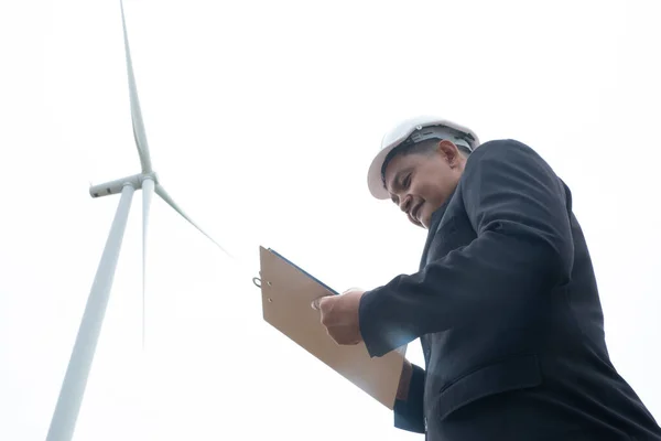 Engineers windmills wearing face mask and  working on clipboard against wind turbine