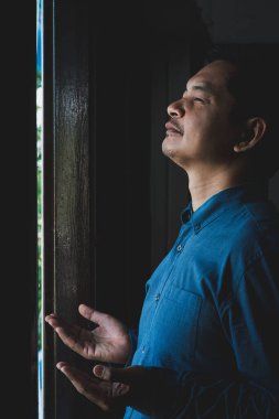 Asyalı adam karanlık odada Tanrı 'ya şükür etmek için dua ediyor.