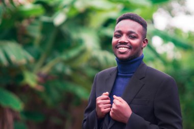 Yakışıklı Afrikalı iş adamı modaya uygun siyah takım elbise içinde duruyor. Mavi uzun kollu ya da kazaklı sakallı adam.