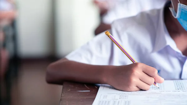 Covid-19 'u korumak için maske takan öğrenciler ve sınıfta stres altında muayene oluyorlar. 16: 9 stili.