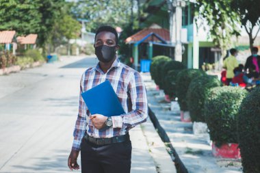 Okulda maskeli neşeli Afrikalı öğretmenin portresi.