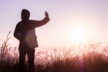 Gezgin adam kazak giyer dağın tepesinde akıllı bir telefonla fotoğraf çeker.