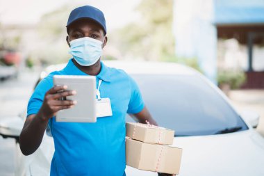 Afrikalı kurye elinde kutular ve yüz maskesi takan tablet tutuyor.