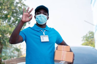 Afrikalı kurye elinde kutular ve maske takan mukavva tutuyor.