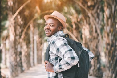 Sırt çantası taşıyan Afrikalı bir gezgin parkta yürüyor.