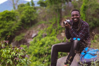 Sırt çantalı Afrikalı gezgin dağların tepesinde fotoğraf çekiyor.