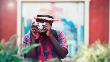 Afrikalı turist, şehirde klasik kamera kullanarak mutlu bir şekilde gülümsüyor.