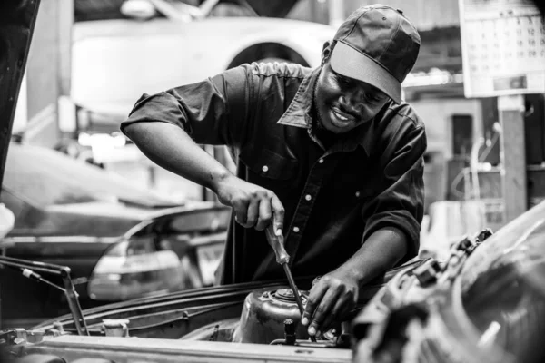 Afrikalı tamirci garajdaki lastik servisini kontrol ediyor. Siyah ve beyaz stili.