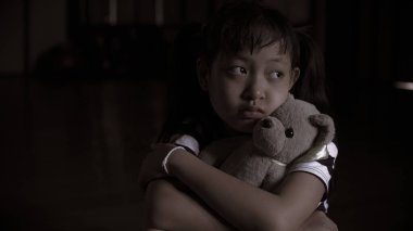 Yalnız küçük kız oyuncak ayısına sarılıyor ve üzgün. Ya da karanlık odada ağlıyor.