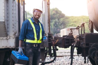 Kask, koruluk ve güvenlik yeleği giyen Afrikalı makine mühendisi treni tamir etmek için İngiliz anahtarı kullanıyor.