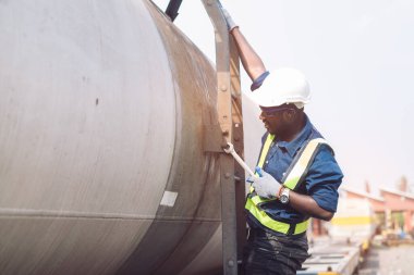 Miğfer, koruluk ve güvenlik yeleği giyen Afrikalı makine mühendisi, tren nakil gazı ve petrol nakil aracını tamir etmek için İngiliz anahtarı kullanıyor.