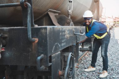 Kask, koruluk ve güvenlik yeleği giyen Afrikalı makine mühendisi treni tamir etmek için İngiliz anahtarı kullanıyor.